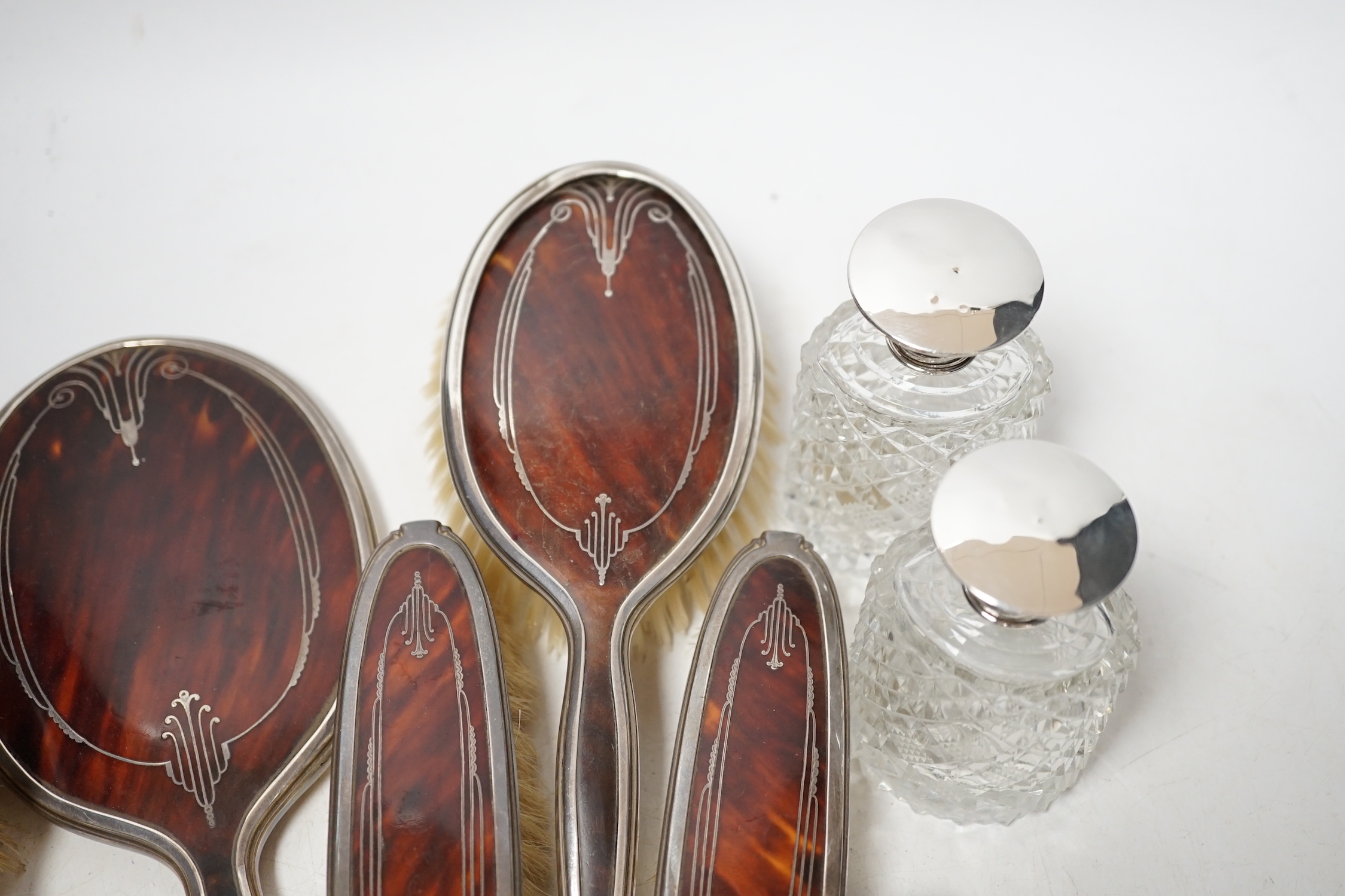 A George V silver and tortoiseshell pique mounted dressing table set, Adie Bros, Birmingham, 1934, and three silver topped toilet jars.